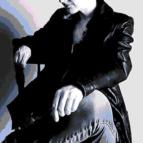 Pixel-art style grey-scale picture of the author with highlights of blue. Wearing leather jacket and jeans, one arm resting on back of a wooden chair, the other on crossed leg. Only part of face is visible.