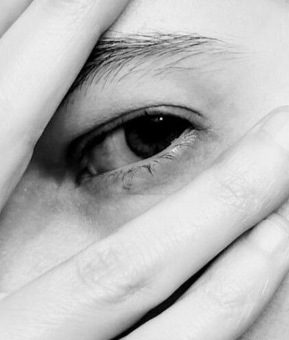 Black and white image of Ella, focusing on the eye. Fingers obscure part of the eyebrow and the cheek.